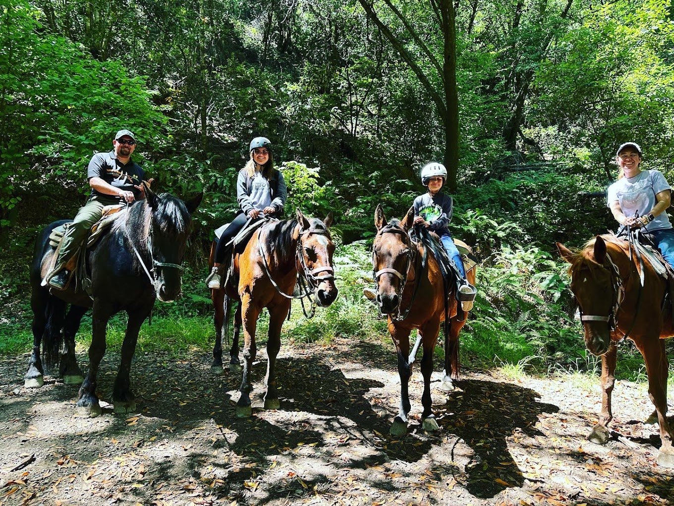 Family Smiling On Horseback In Woods