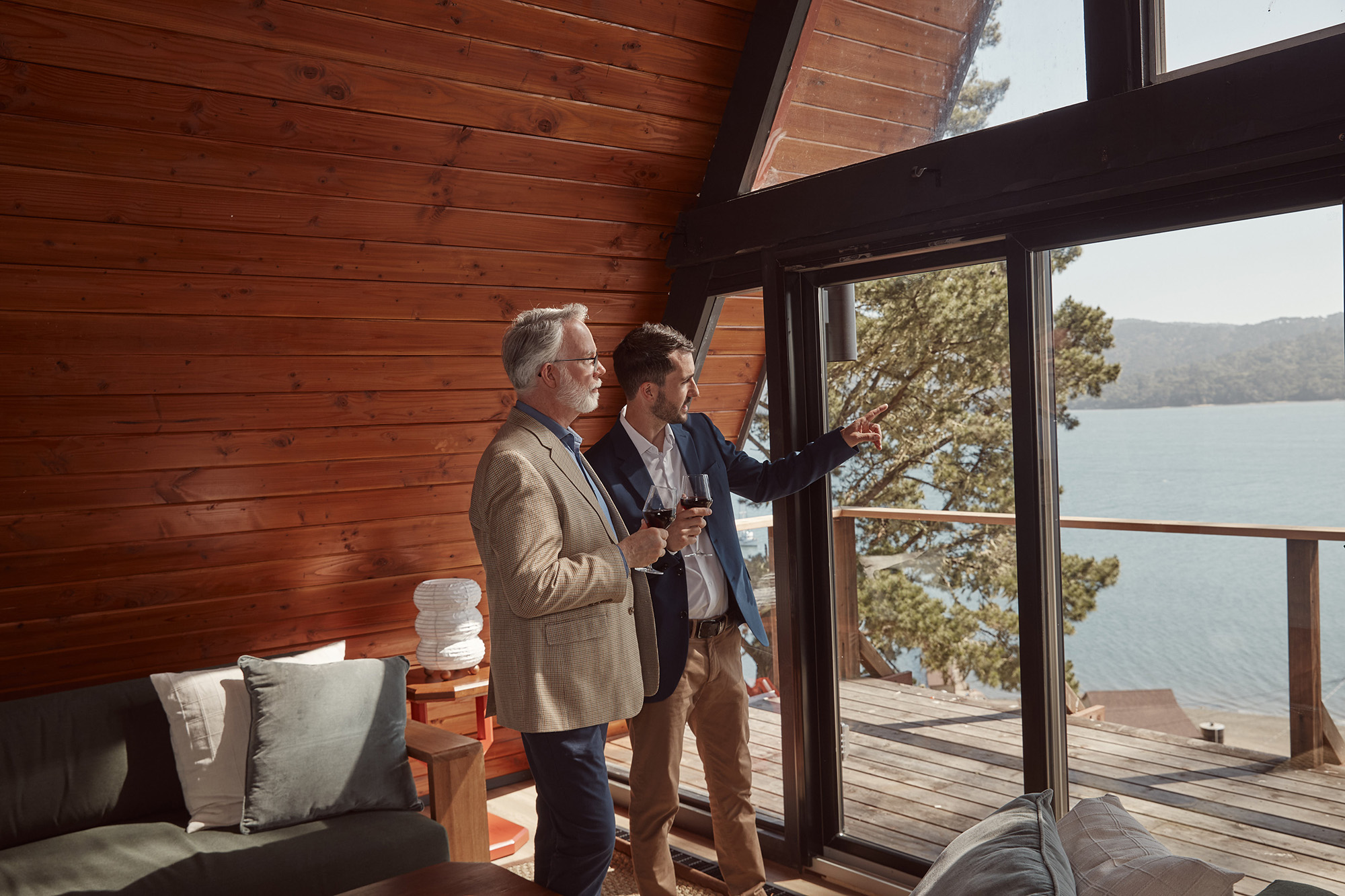 photo of two men with wine glasses looking at the floor to ceiling windows of the a-frame